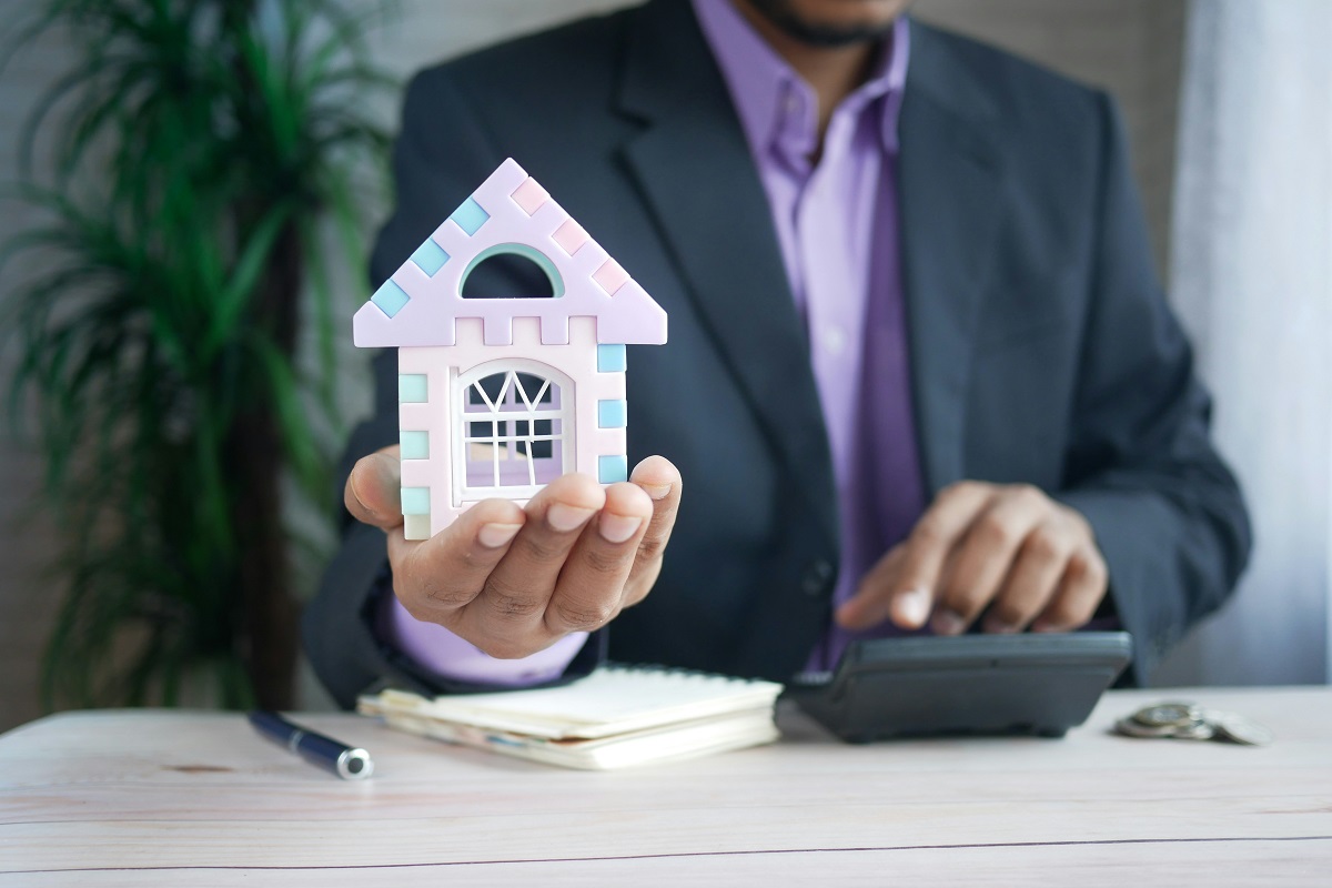 insurance agent holding a miniature house while using a calculator